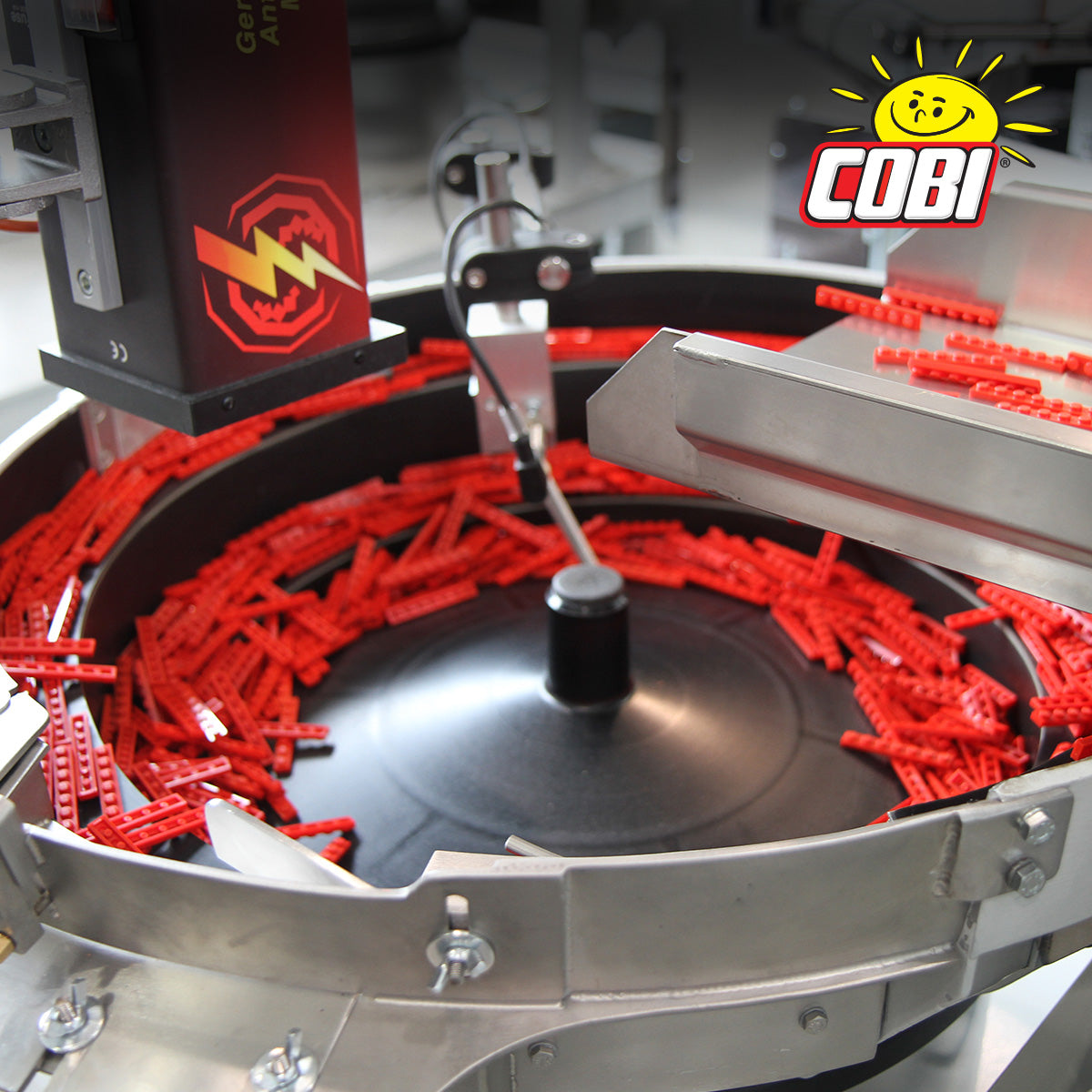 Primer plano de una máquina circular transportadora o clasificadora llena de numerosos bloques de construcción de plástico rojo brillante. La máquina está hecha de metal plateado, con un buje central negro y una unidad de rodillos roja y negra con marca a la izquierda.